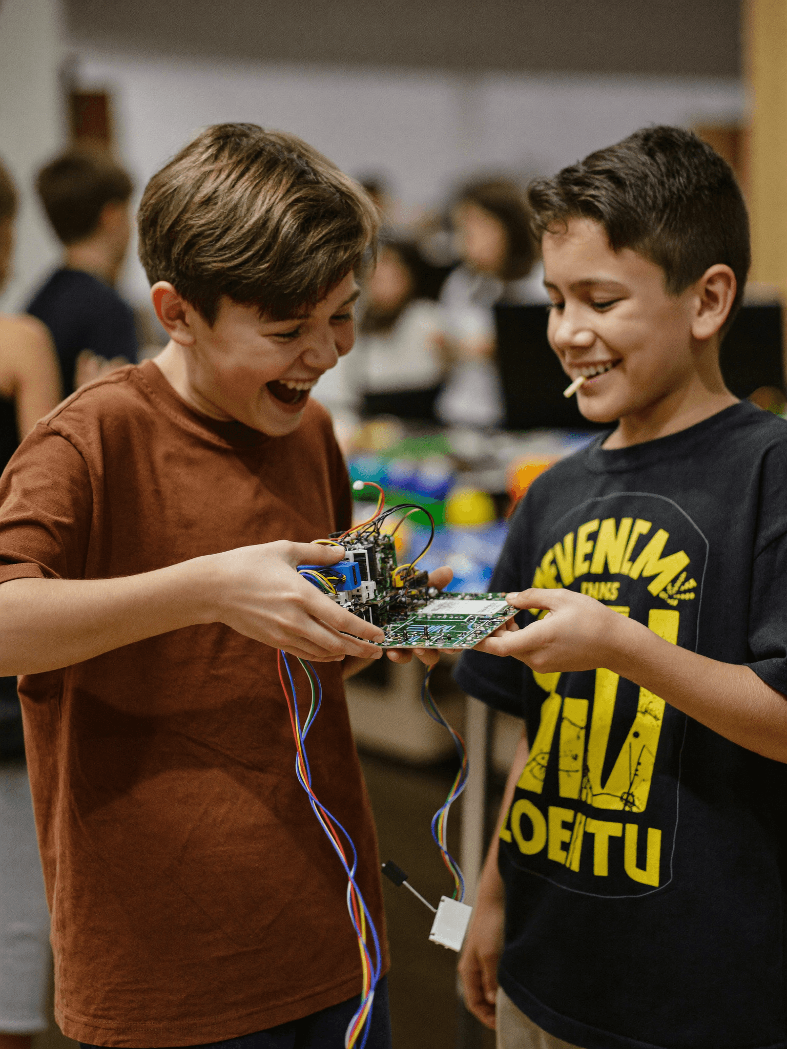Two boys laughing while holding a circuit board and motors